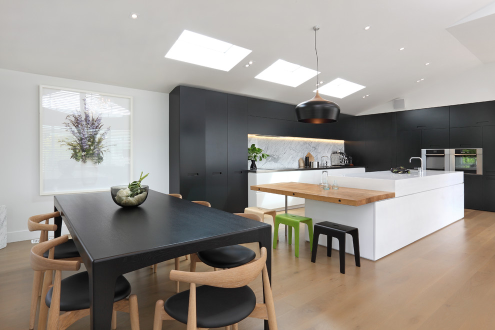 This is an example of a contemporary eat-in kitchen in Auckland with stainless steel appliances, wood benchtops, flat-panel cabinets, white splashback and stone slab splashback.
