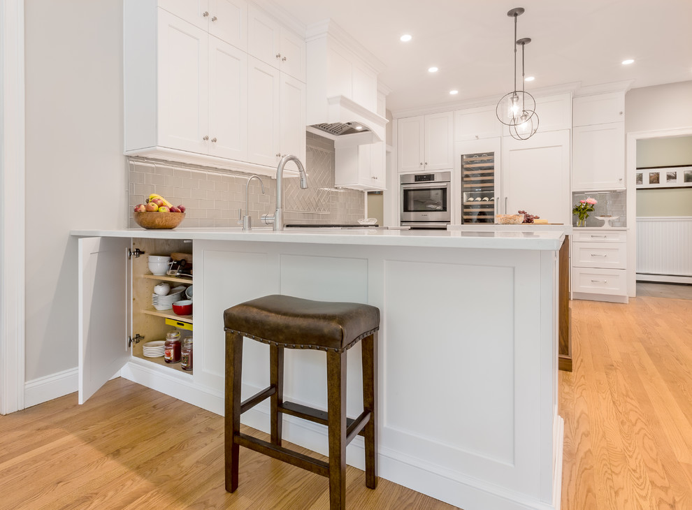 Eat-in kitchen - large transitional u-shaped light wood floor and brown floor eat-in kitchen idea in Boston with an undermount sink, recessed-panel cabinets, white cabinets, quartz countertops, gray backsplash, glass tile backsplash, stainless steel appliances, an island and white countertops