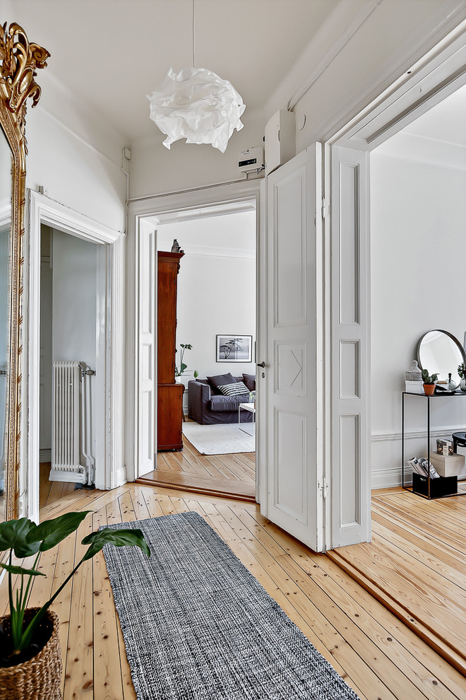 Design ideas for a large scandinavian hallway in Stockholm with white walls and light hardwood floors.