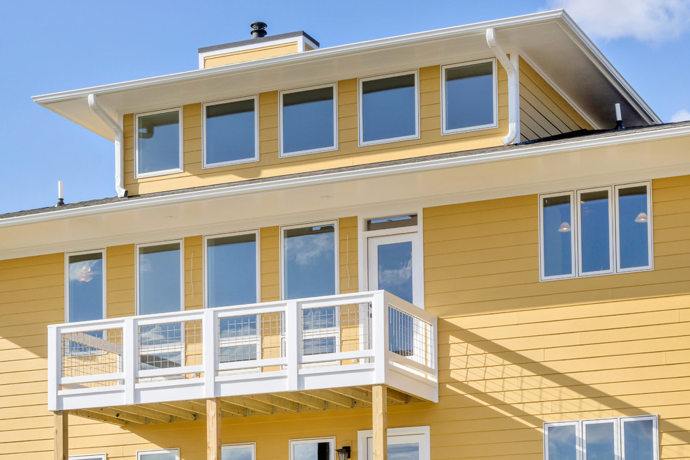 This is an example of a large arts and crafts three-storey yellow exterior in Other with wood siding and a flat roof.