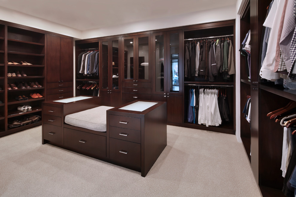Transitional men's dressing room in Orange County with dark wood cabinets, carpet, beige floor and open cabinets.