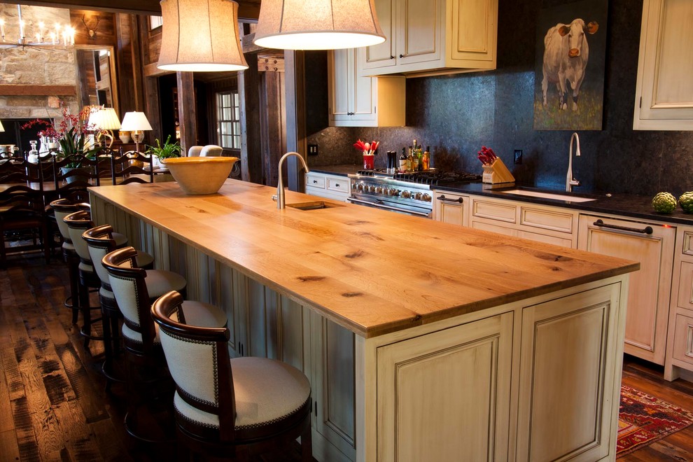 Example of a mid-sized mountain style galley medium tone wood floor and brown floor eat-in kitchen design in Other with an undermount sink, recessed-panel cabinets, white cabinets, wood countertops, black backsplash, stainless steel appliances, an island and beige countertops