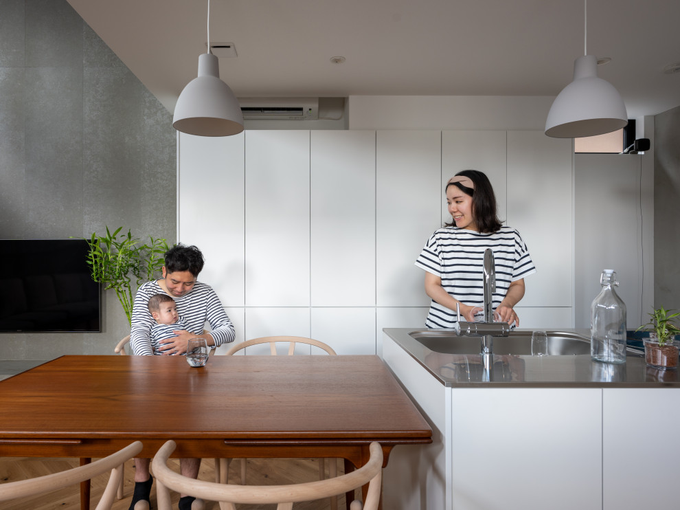 Small scandinavian grey and white open plan kitchen in Other with flat-panel cabinets, white cabinets, stainless steel worktops, grey splashback, stone tiled splashback, plywood flooring, an island, brown floors, white worktops, a wallpapered ceiling, an integrated sink and white appliances.