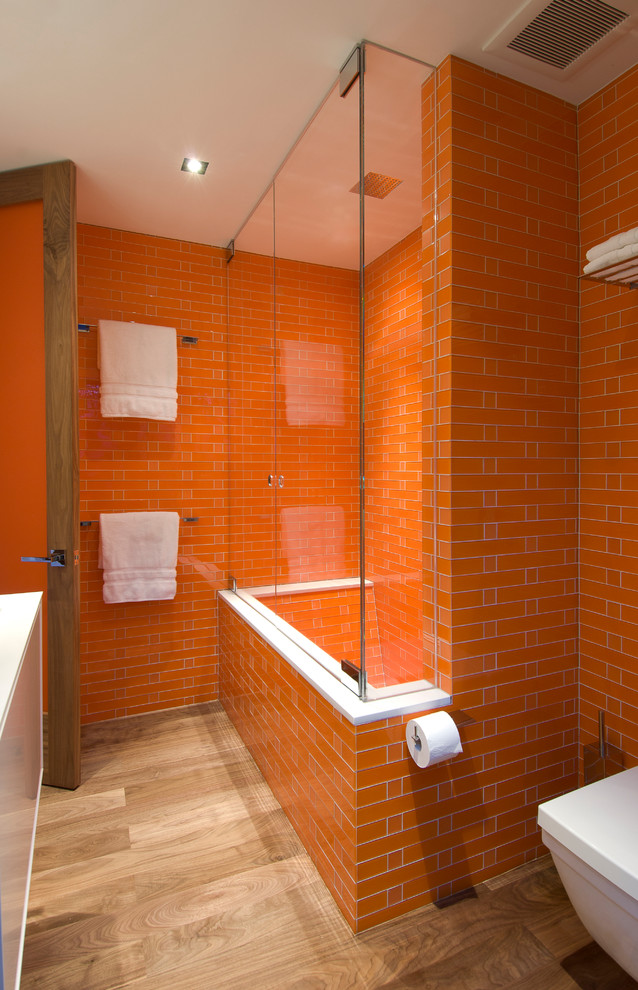 This is an example of a mid-sized modern kids bathroom in Los Angeles with an alcove tub, a shower/bathtub combo, orange tile, orange walls, light hardwood floors, beige floor, a hinged shower door and recessed.