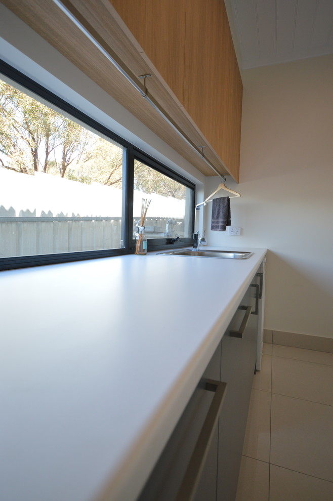 This is an example of a mid-sized modern l-shaped dedicated laundry room in Adelaide with a single-bowl sink, light wood cabinets, laminate benchtops, white walls and porcelain floors.