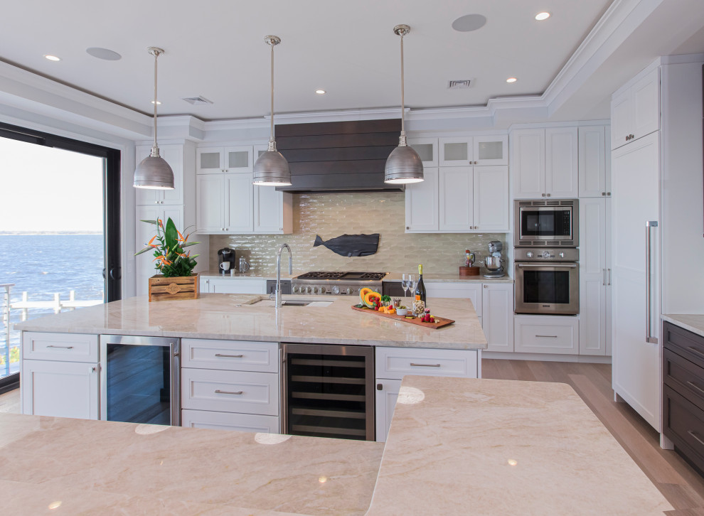 Large transitional l-shaped open plan kitchen in New York with an undermount sink, recessed-panel cabinets, yellow cabinets, quartzite benchtops, beige splashback, cement tile splashback, stainless steel appliances, medium hardwood floors, multiple islands, beige floor and beige benchtop.