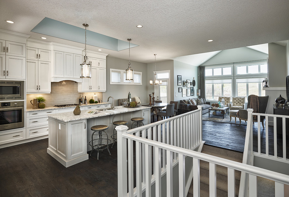 Open concept kitchen - mid-sized transitional l-shaped dark wood floor open concept kitchen idea in Calgary with an undermount sink, recessed-panel cabinets, white cabinets, granite countertops, beige backsplash, ceramic backsplash, stainless steel appliances and an island