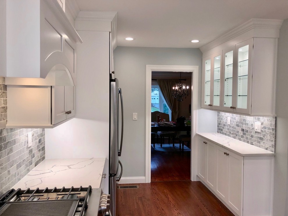 Example of a mid-sized transitional u-shaped dark wood floor and brown floor enclosed kitchen design with an undermount sink, shaker cabinets, white cabinets, marble countertops, gray backsplash, stone tile backsplash, stainless steel appliances, no island and white countertops