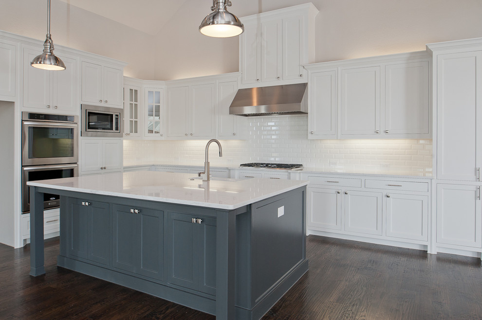 Example of a large transitional l-shaped dark wood floor open concept kitchen design in Dallas with a farmhouse sink, shaker cabinets, white cabinets, granite countertops, white backsplash, subway tile backsplash, stainless steel appliances and an island