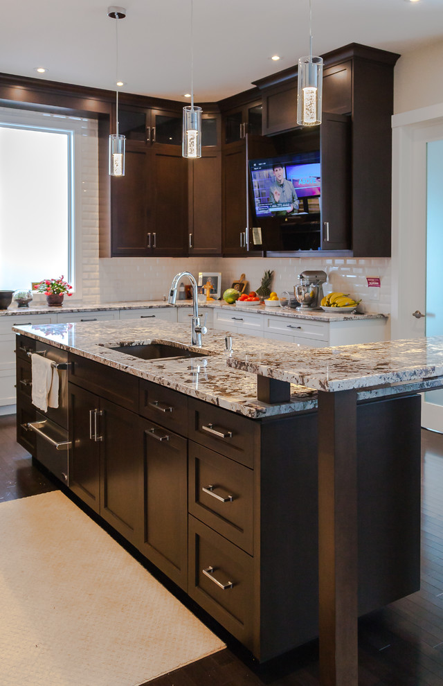 Example of a large transitional u-shaped dark wood floor and brown floor kitchen design in Calgary with an undermount sink, shaker cabinets, white cabinets, granite countertops, white backsplash, subway tile backsplash, stainless steel appliances and an island