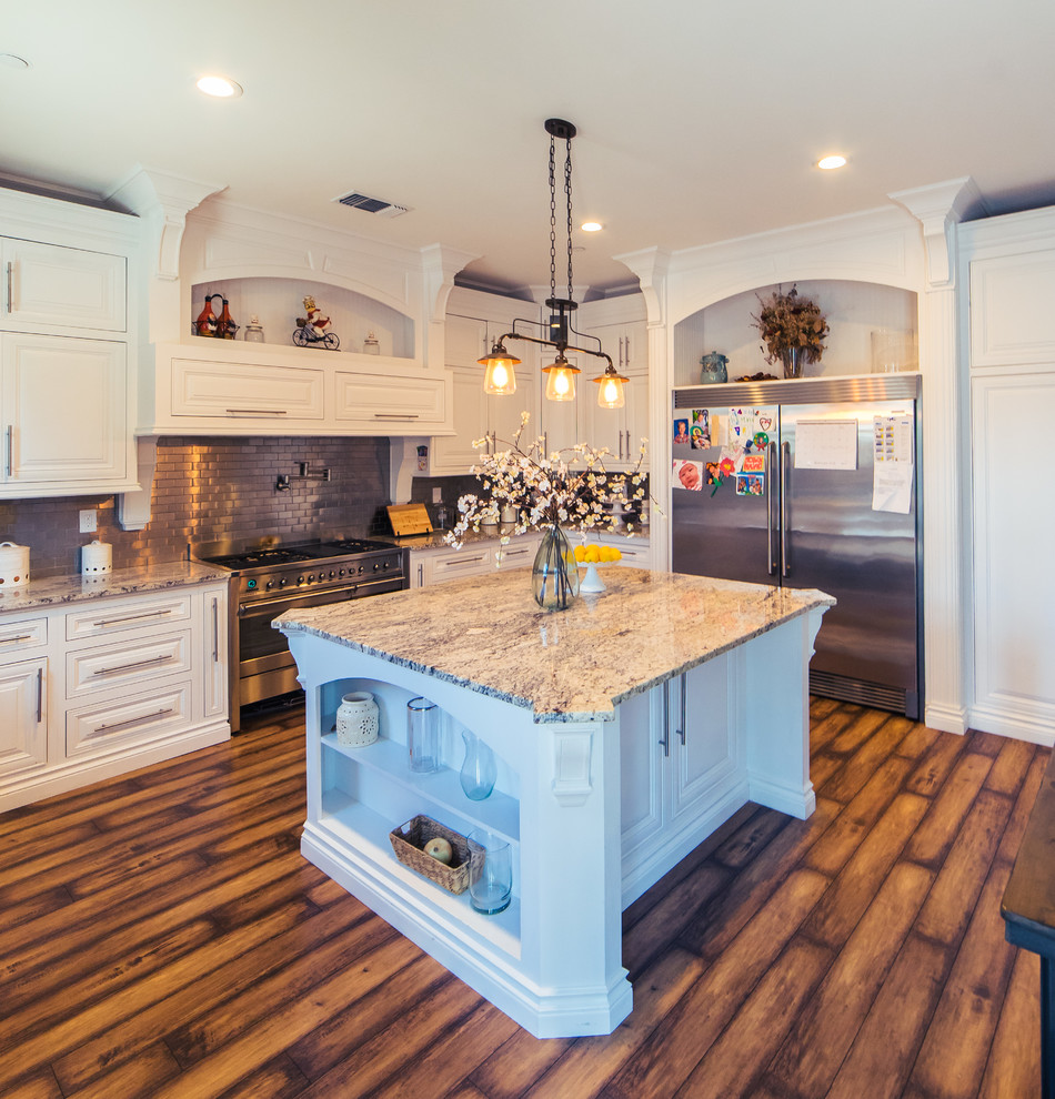 This is an example of a large country u-shaped separate kitchen in Sacramento with a farmhouse sink, raised-panel cabinets, white cabinets, granite benchtops, metallic splashback, metal splashback, stainless steel appliances, dark hardwood floors, with island, brown floor and brown benchtop.
