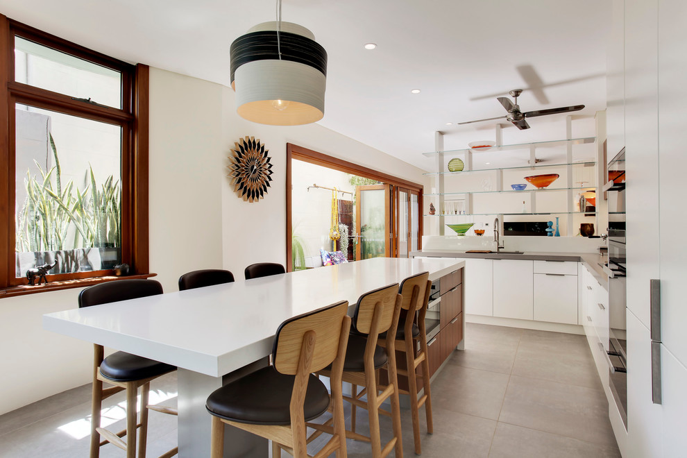 Design ideas for a large contemporary l-shaped open plan kitchen in Sydney with an undermount sink, flat-panel cabinets, white cabinets, quartz benchtops, grey splashback, mirror splashback, black appliances, concrete floors and with island.