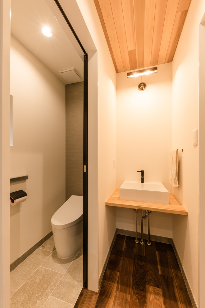 This is an example of a small modern powder room in Other with white walls, dark hardwood floors, a vessel sink, wood benchtops, brown floor and beige benchtops.