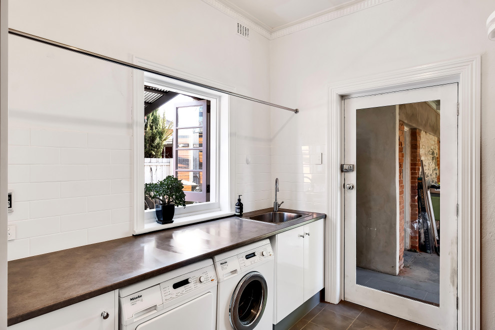 Design ideas for a contemporary single-wall dedicated laundry room in Adelaide with a drop-in sink, flat-panel cabinets, white cabinets, white splashback, subway tile splashback, white walls, a side-by-side washer and dryer, brown floor and brown benchtop.