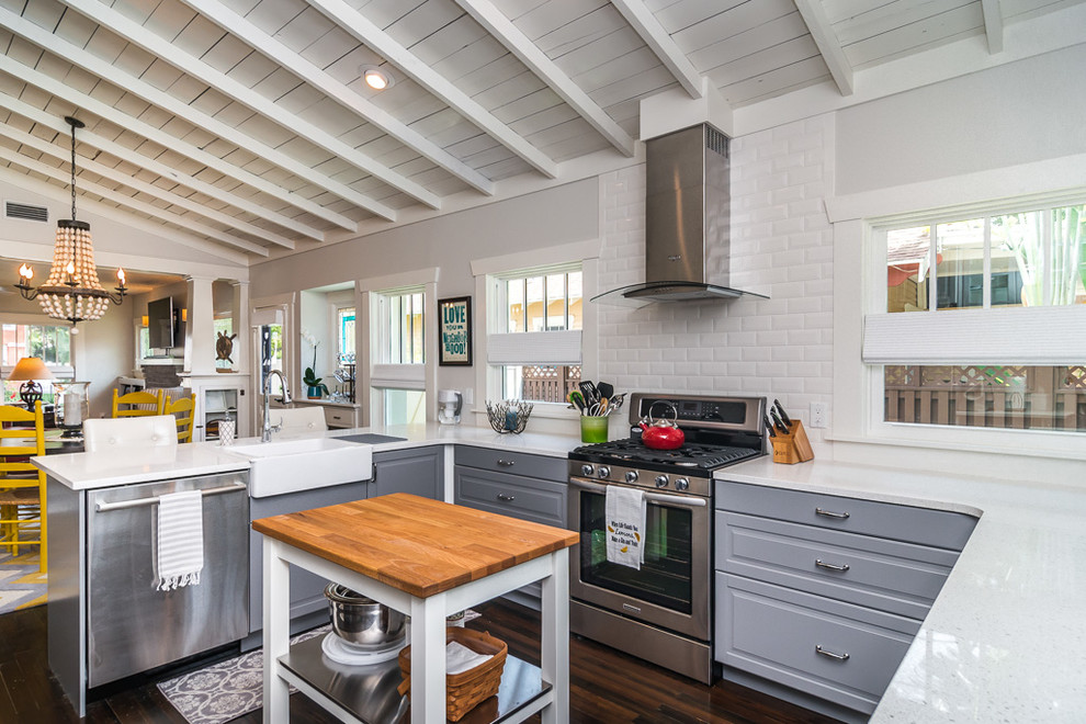 Traditional u-shaped open plan kitchen in Tampa with a farmhouse sink, raised-panel cabinets, grey cabinets, white splashback, subway tile splashback, stainless steel appliances, dark hardwood floors and with island.