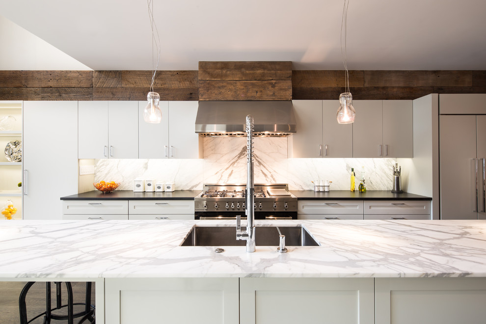 Inspiration for a transitional galley kitchen in New York with a single-bowl sink, flat-panel cabinets, white cabinets, grey splashback, stainless steel appliances, medium hardwood floors, with island, brown floor and grey benchtop.
