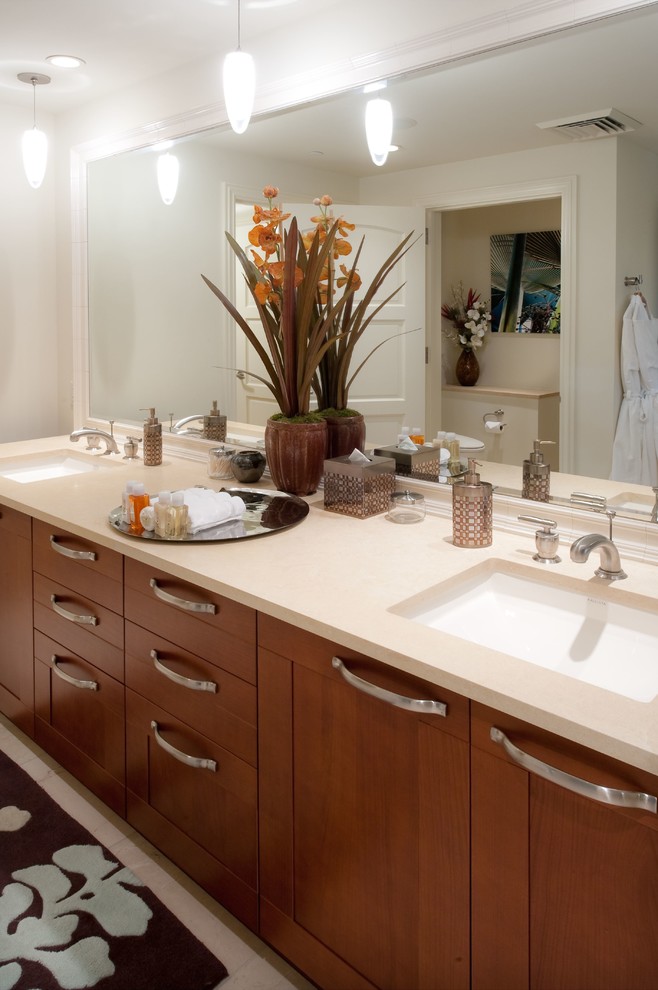This is an example of a tropical master bathroom in Hawaii with shaker cabinets, brown cabinets, a drop-in tub, a curbless shower, a one-piece toilet, beige tile, stone tile, beige walls, limestone floors, an undermount sink and limestone benchtops.