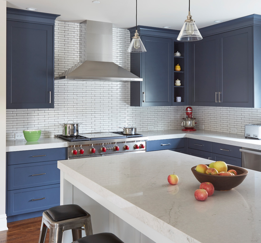 Example of a mid-sized transitional u-shaped medium tone wood floor and brown floor enclosed kitchen design in Chicago with blue cabinets, quartz countertops, white backsplash, ceramic backsplash, stainless steel appliances, an island, an undermount sink, shaker cabinets and white countertops