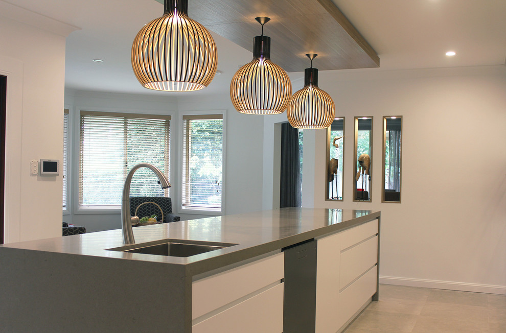 Photo of a large contemporary single-wall open plan kitchen in Sydney with an undermount sink, flat-panel cabinets, white cabinets, quartz benchtops, grey splashback, black appliances, porcelain floors, with island, grey floor and grey benchtop.