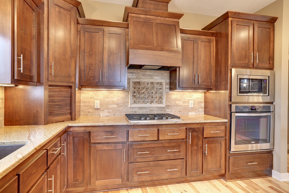Inspiration for a mid-sized traditional u-shaped open plan kitchen in Minneapolis with an undermount sink, shaker cabinets, dark wood cabinets, granite benchtops, beige splashback, stone tile splashback, stainless steel appliances, medium hardwood floors and with island.