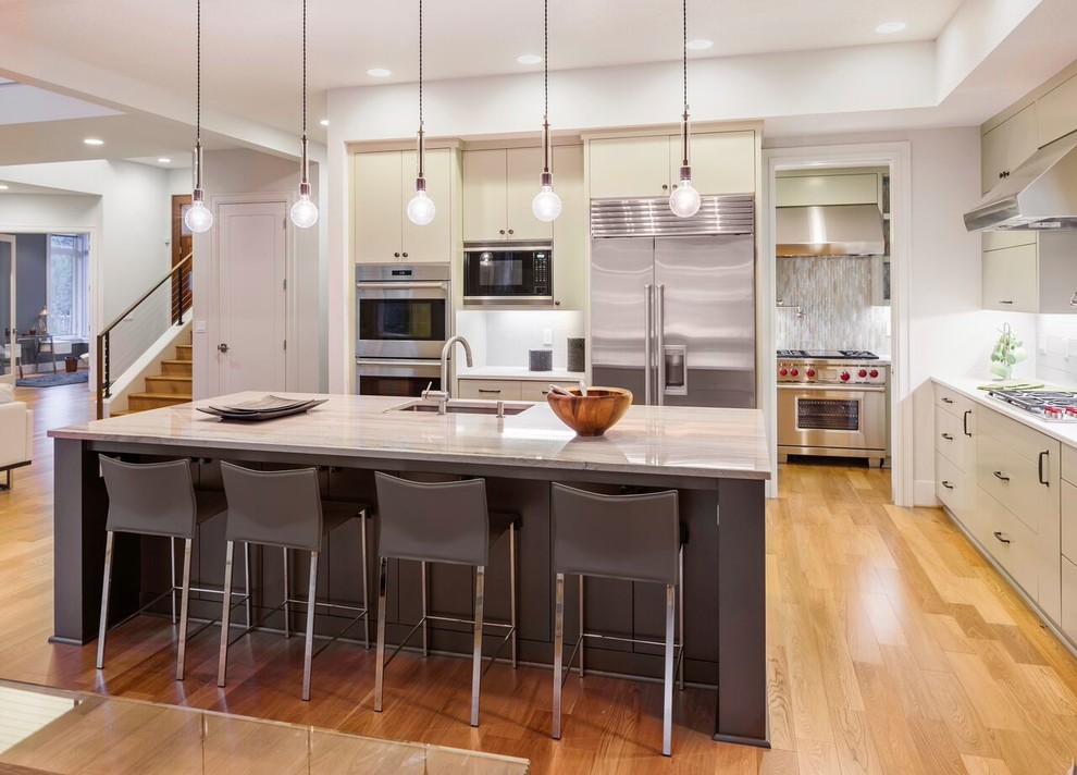 This is an example of a mid-sized contemporary galley open plan kitchen in DC Metro with an undermount sink, stainless steel appliances, medium hardwood floors, with island, flat-panel cabinets, beige cabinets, grey splashback, matchstick tile splashback, beige floor and quartzite benchtops.