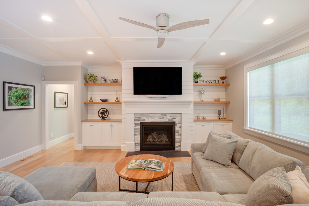 This is an example of a contemporary open plan games room in Boston with light hardwood flooring, a standard fireplace, a stacked stone fireplace surround, a wall mounted tv and a coffered ceiling.