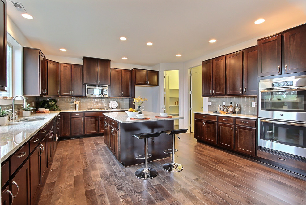 Inspiration for a large transitional u-shaped dark wood floor kitchen remodel in Seattle with an undermount sink, recessed-panel cabinets, dark wood cabinets, granite countertops, gray backsplash, glass tile backsplash, stainless steel appliances, white walls and an island