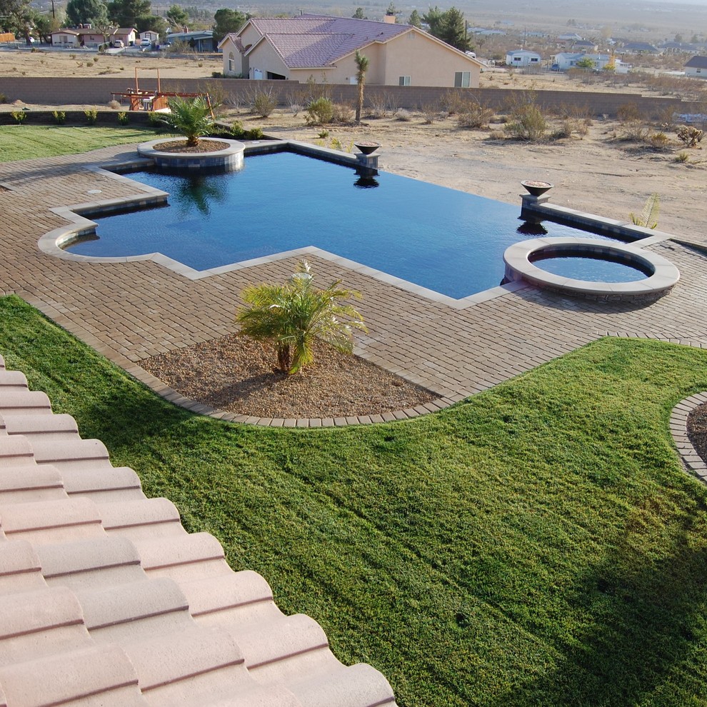 Mid-sized traditional backyard custom-shaped infinity pool in Los Angeles with concrete pavers.