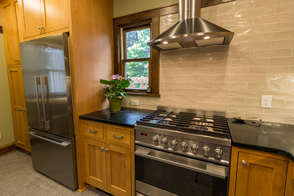 Photo of an arts and crafts kitchen in Minneapolis with an undermount sink, flat-panel cabinets, medium wood cabinets, soapstone benchtops, beige splashback, stainless steel appliances, linoleum floors, no island and beige floor.