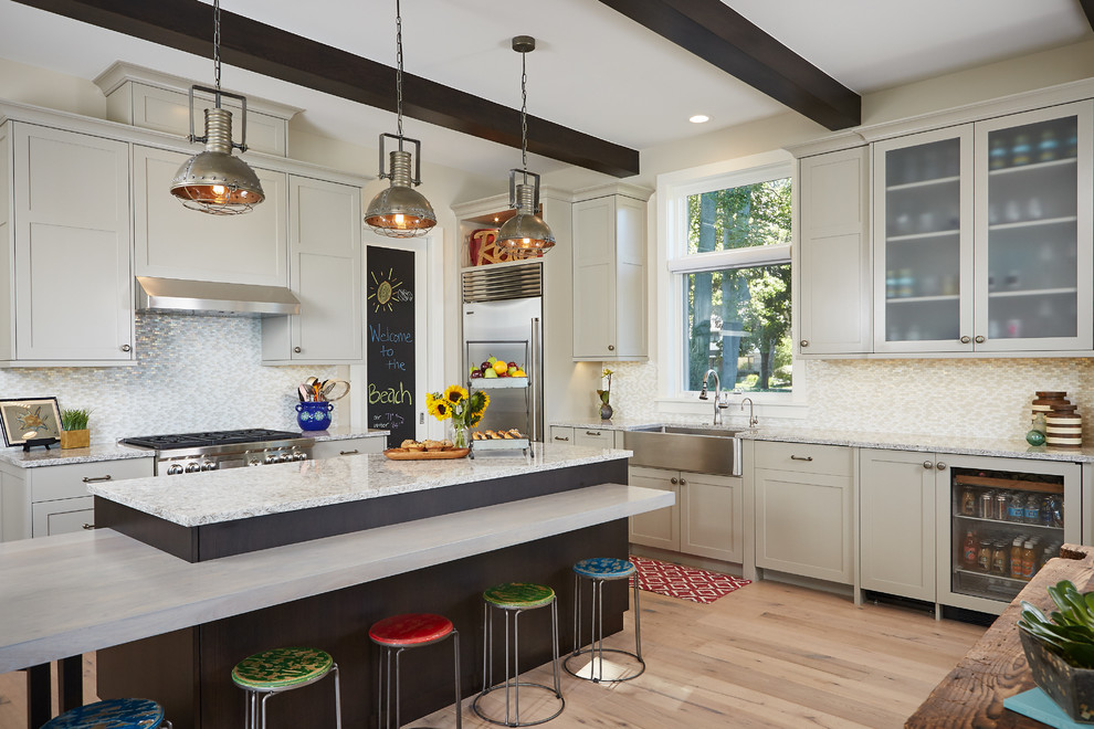Beach style kitchen in Grand Rapids with a farmhouse sink, glass-front cabinets, beige cabinets, metallic splashback, mosaic tile splashback, stainless steel appliances, light hardwood floors and with island.