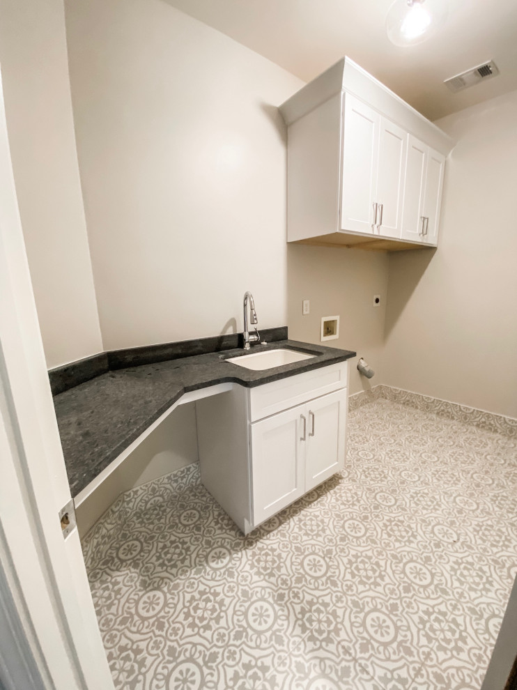 This is an example of a mid-sized transitional l-shaped dedicated laundry room in Atlanta with a drop-in sink, shaker cabinets, white cabinets, granite benchtops, grey walls, porcelain floors, a side-by-side washer and dryer, grey floor and black benchtop.