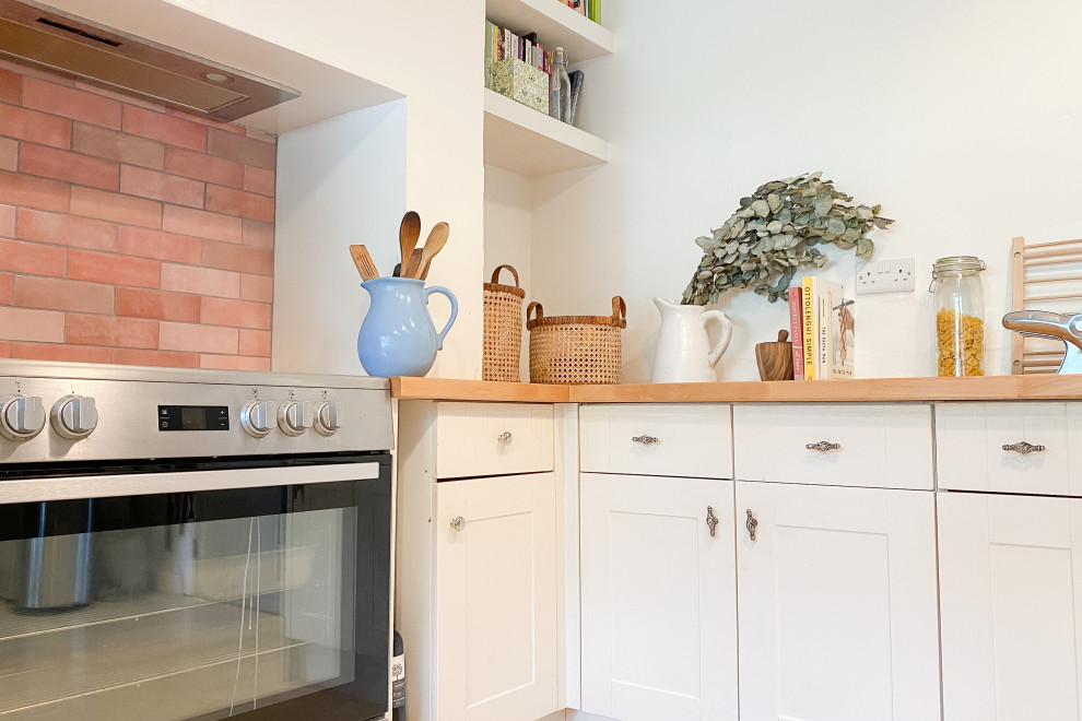 This is an example of a mid-sized traditional u-shaped eat-in kitchen in Cornwall with a farmhouse sink, shaker cabinets, beige cabinets, wood benchtops, pink splashback, ceramic splashback, stainless steel appliances, limestone floors, no island, beige floor and brown benchtop.