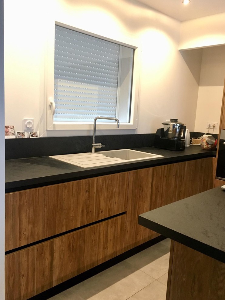 Mid-sized industrial l-shaped open plan kitchen in Grenoble with a single-bowl sink, medium wood cabinets, laminate benchtops, black splashback, panelled appliances, with island, grey floor and black benchtop.
