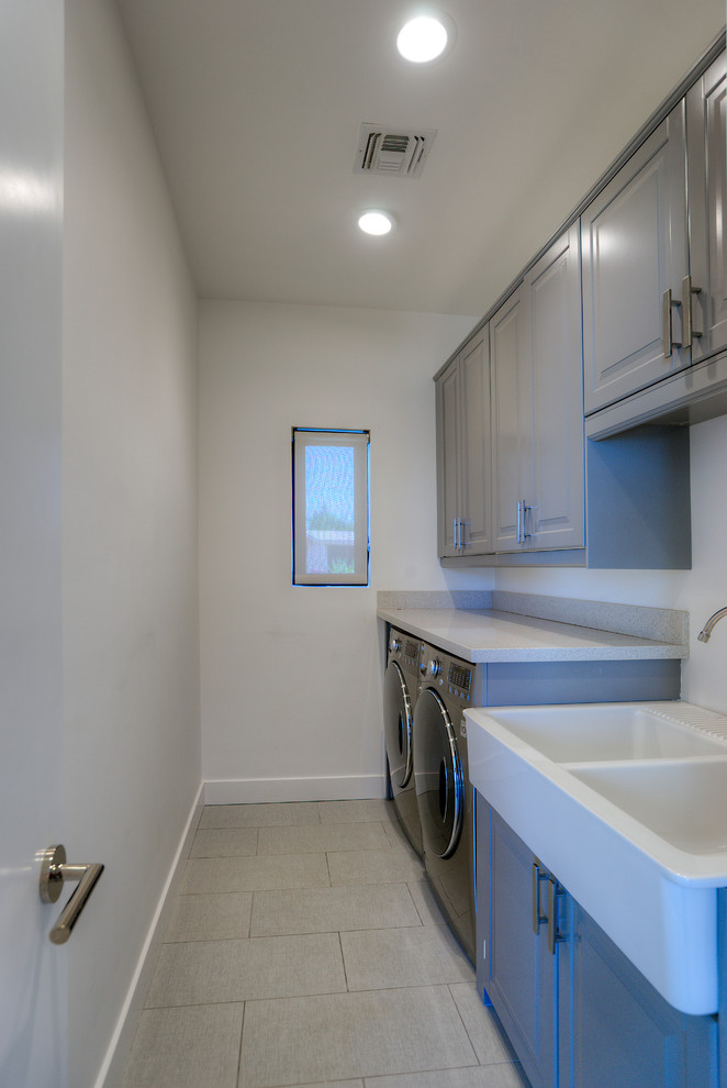 This is an example of a mid-sized transitional laundry room with an utility sink, raised-panel cabinets, grey cabinets, grey walls and a side-by-side washer and dryer.