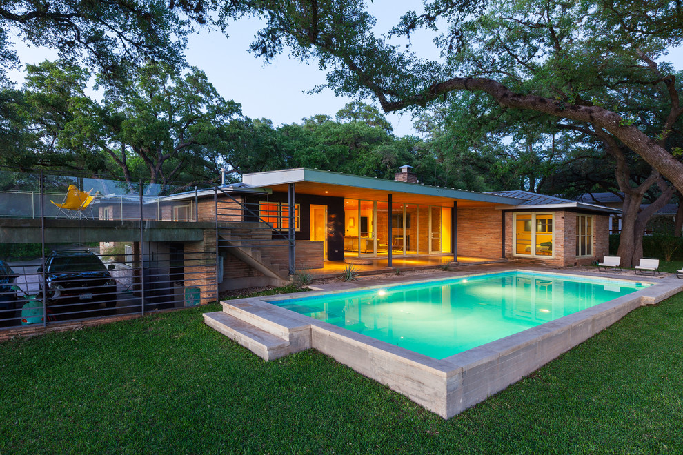 Large midcentury backyard rectangular lap pool in Austin with concrete slab.