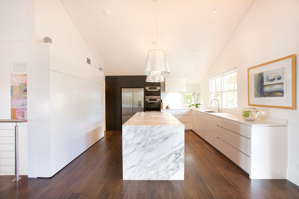 Photo of a large contemporary kitchen in Sydney with an undermount sink, quartz benchtops, white splashback, glass sheet splashback, stainless steel appliances, with island, flat-panel cabinets, white cabinets and dark hardwood floors.