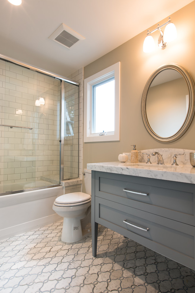 Inspiration for a small beach style bathroom in Orange County with recessed-panel cabinets, blue cabinets, a freestanding tub, a shower/bathtub combo, a one-piece toilet, white tile, ceramic tile, beige walls, mosaic tile floors, an undermount sink and marble benchtops.