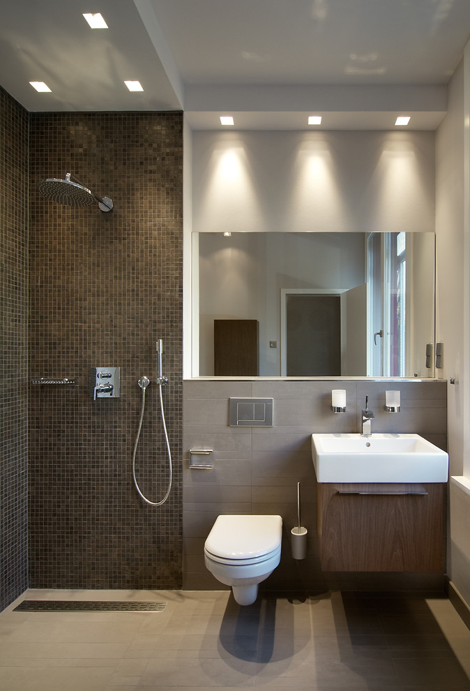 Design ideas for a mid-sized contemporary 3/4 bathroom in Berlin with flat-panel cabinets, dark wood cabinets, an open shower, a wall-mount toilet, brown tile, mosaic tile, grey walls, a vessel sink and an open shower.