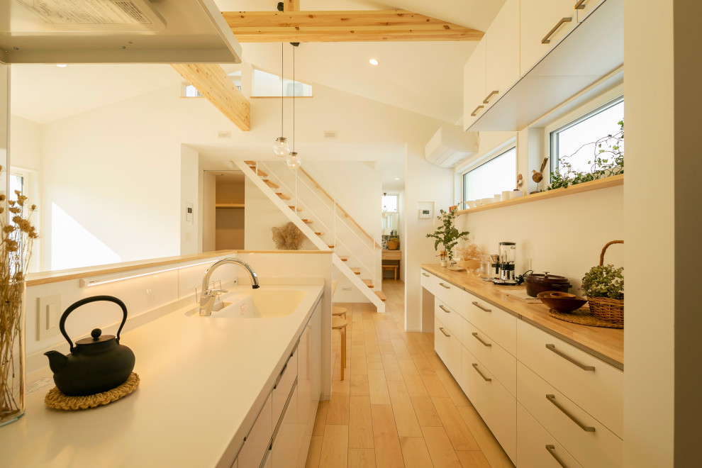 Inredning av ett nordiskt mellanstort beige linjärt beige kök med öppen planlösning, med en undermonterad diskho, vita skåp, bänkskiva i koppar, vitt stänkskydd, ljust trägolv och beiget golv