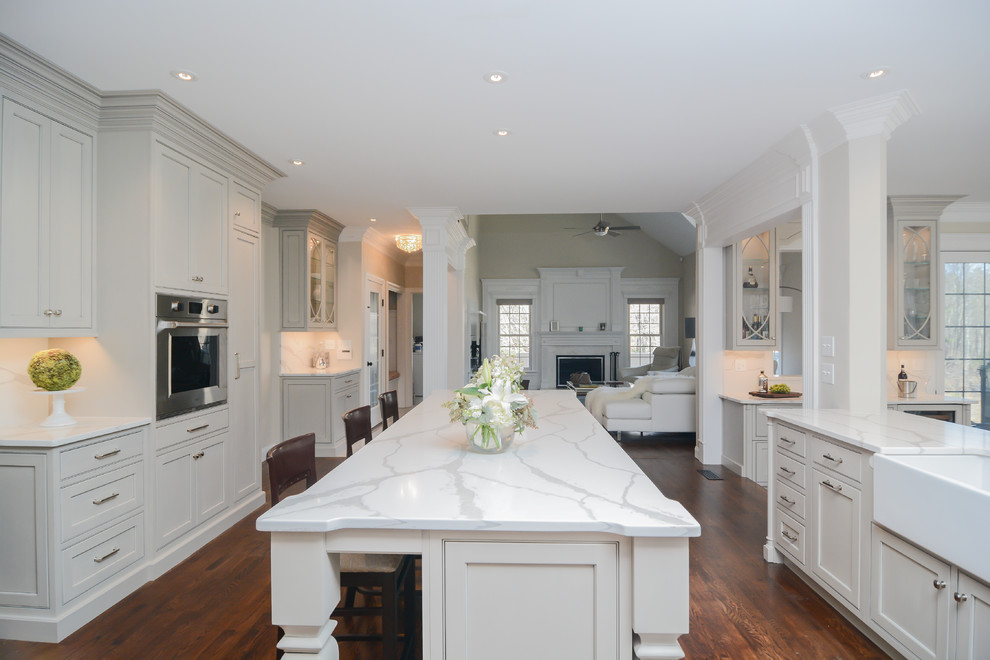 Photo of an expansive traditional u-shaped open plan kitchen in Boston with a farmhouse sink, beaded inset cabinets, grey cabinets, quartz benchtops, white splashback, stone slab splashback, stainless steel appliances, medium hardwood floors, multiple islands and white benchtop.