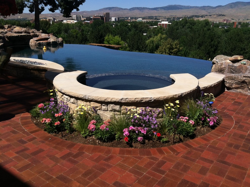 This is an example of a mid-sized modern backyard custom-shaped infinity pool in Boise with a hot tub and brick pavers.