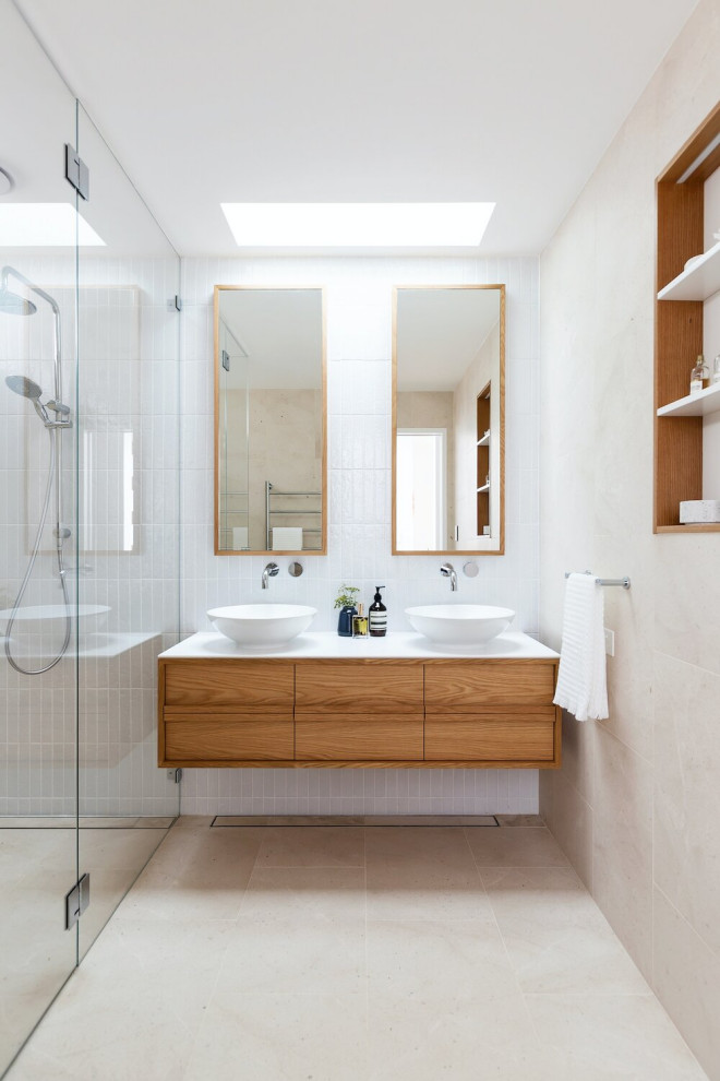 This is an example of a mid-sized beach style bathroom in Sydney with medium wood cabinets, white tile, ceramic tile, ceramic floors, a vessel sink, quartzite benchtops, beige floor, a hinged shower door, white benchtops, a double vanity, a floating vanity, flat-panel cabinets, a curbless shower and beige walls.