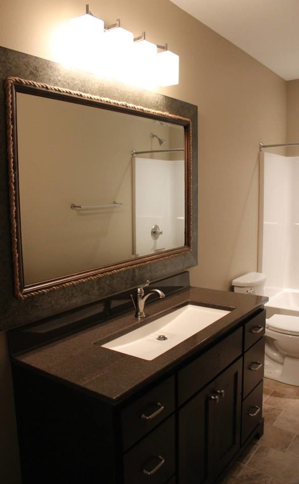 Large transitional 3/4 white tile and stone slab dark wood floor corner bathtub photo with raised-panel cabinets, dark wood cabinets, a one-piece toilet, gray walls, a pedestal sink and granite countertops