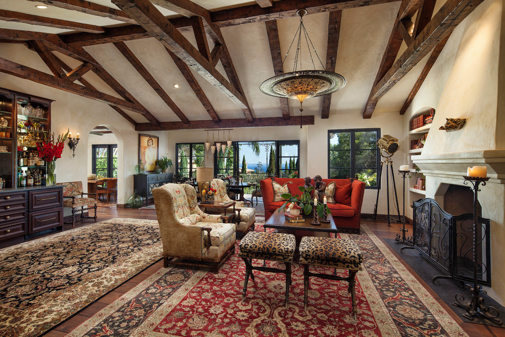 This is an example of a large mediterranean enclosed living room in Santa Barbara with a home bar, beige walls, a standard fireplace, a plaster fireplace surround, no tv and medium hardwood floors.