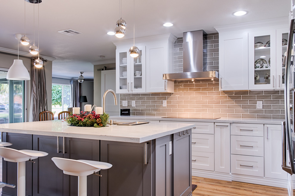 Example of a mid-sized transitional l-shaped laminate floor open concept kitchen design in Phoenix with an undermount sink, shaker cabinets, white cabinets, quartzite countertops, gray backsplash, ceramic backsplash, stainless steel appliances and an island