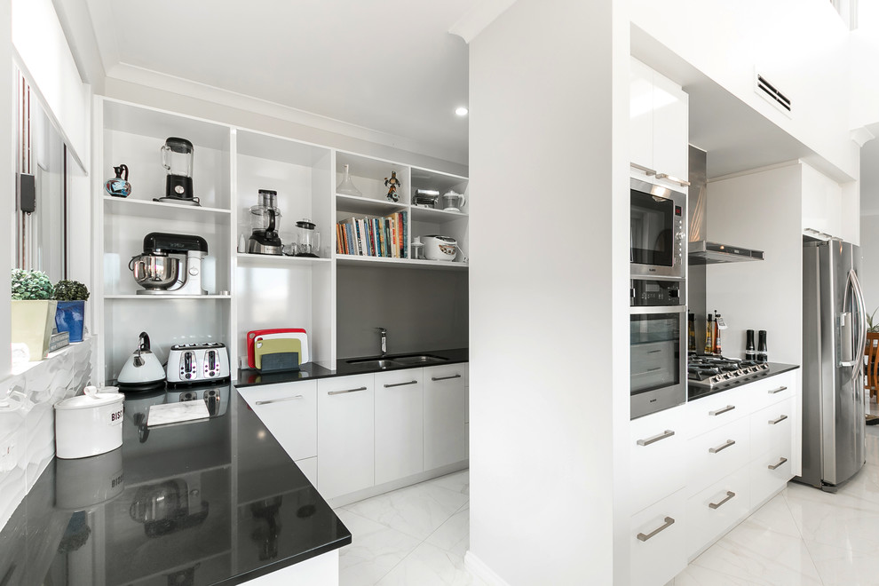 Large modern u-shaped kitchen pantry in Perth with a drop-in sink, beaded inset cabinets, white cabinets, granite benchtops, grey splashback, stainless steel appliances, porcelain floors, multiple islands, white floor and black benchtop.