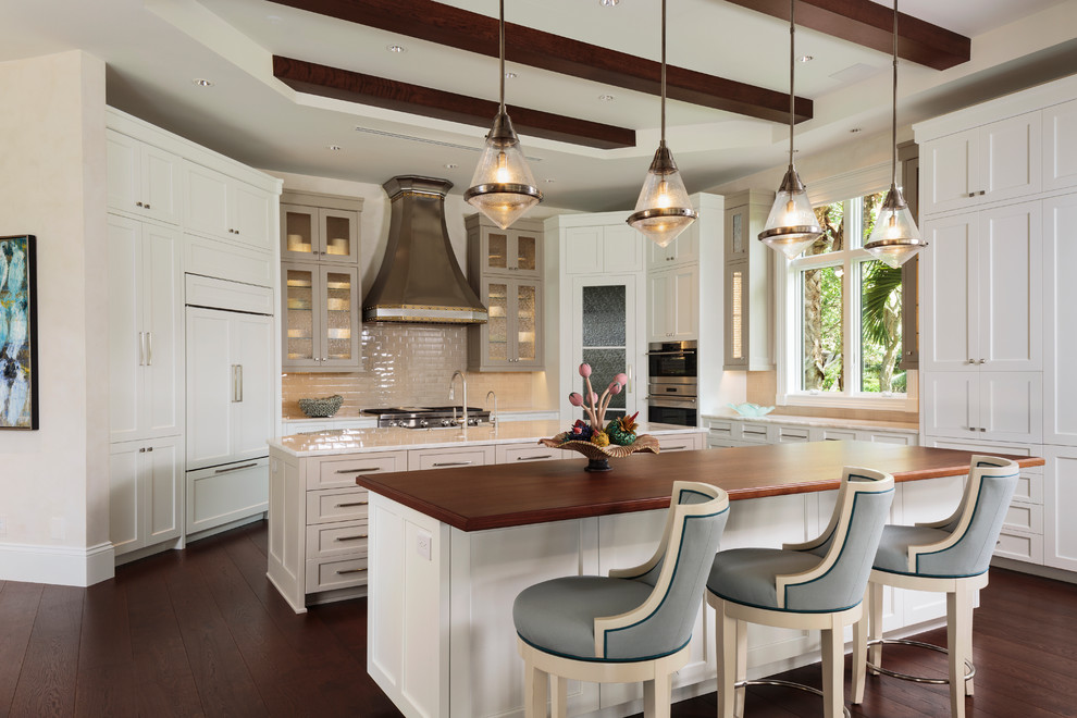 This is an example of a transitional galley kitchen in Miami with shaker cabinets, white cabinets, wood benchtops, beige splashback, subway tile splashback, dark hardwood floors, multiple islands, brown floor and brown benchtop.
