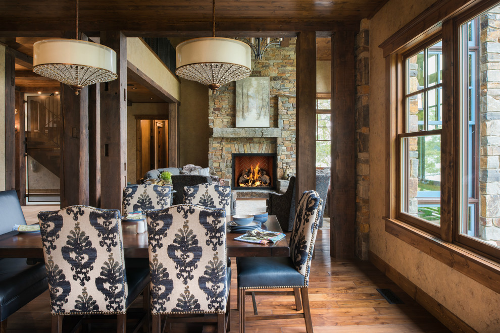Example of a large mountain style medium tone wood floor and brown floor kitchen/dining room combo design in Minneapolis with beige walls, a standard fireplace and a stone fireplace