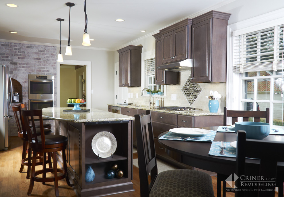 Example of a transitional light wood floor eat-in kitchen design with shaker cabinets, dark wood cabinets, granite countertops, beige backsplash, glass tile backsplash, stainless steel appliances and an island