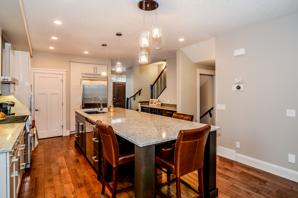 Large transitional l-shaped medium tone wood floor open concept kitchen photo in Calgary with an undermount sink, shaker cabinets, white cabinets, granite countertops, gray backsplash, porcelain backsplash, stainless steel appliances and an island